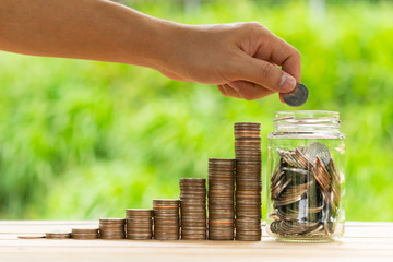 White hand man holding coin to putting in Jar or glass bottle for saving with green background. Saving money, Saving concept