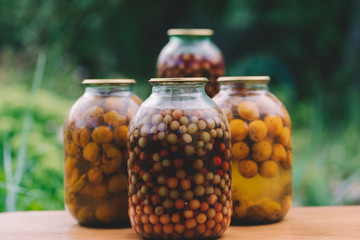 A lot of glass jars of canned fruit are on the street. Jars of pickled fruit in the garden are on the table. Pickled food