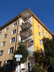 Wohnhaus mit Eckbalkons und Fassade in Gelb und Beige im Sommer bei blauem Himmel und Sonnenschein...