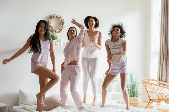 Four Slim Sexy Girls Best Friends Hanging Out Together Dancing Standing Full Length In Bed Listening Music. Multi Ethnic Women Enjoy Bachelorette Party In Pajamas, Bridal Shower Celebration Concept