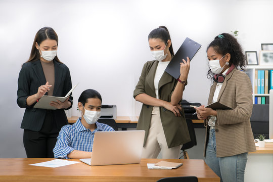 Asian office workers wearing face masks working in the new normal office and doing social distancing during coronavirus COVID-19 pandemic