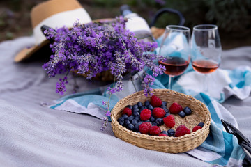 A beautiful picnic in nature with berries, glasses with red wine, a bouquet of lavender and a straw hat. Gorizontal.