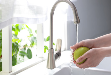 Woman washing apple over sink in kitchen, closeup. Space for text