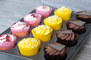 Variety of cupcakes in a metal baking tray.  Grey wood background