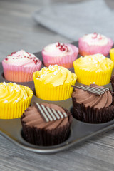 Variety of cupcakes in a metal baking tray.  Grey wood background