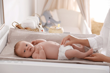Mother changing her baby's diaper on table in room