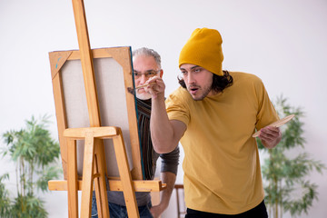 Old man taking lesson from young painter