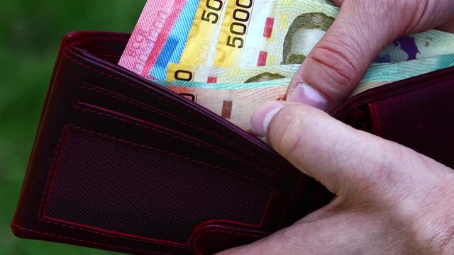 The man is holding a wallet in his hand and is counting money. Currency from Costa Rica, various banknotes. Cash called Colones