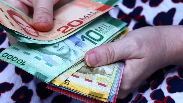 The woman holds in her hand and counts a large amount of Costa Rican money, banknotes of different values  