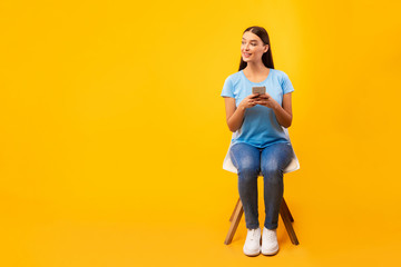 Studio shot of girl sitting on chair with phone