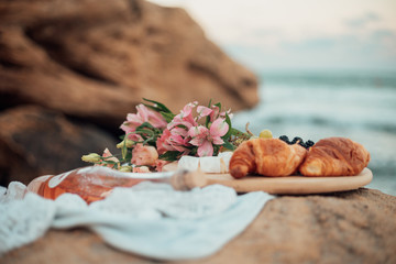 Picnic by the sea. Close-up flowers, croissants and a bottle of wine. Side view.