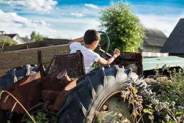 A 10-year-old school-age boy tries to start an old tractor or car. Repair. Little helper. Harvest time. Raising sons by father. Photo. Family farmer