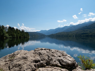 View towards reflecting lake with forest to the left and mountains to the right with rock surface in forefront implying viewer standing on stone