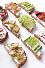 Bruschetta assortment with cream cheese, vegetables, mushrooms and bacon on the white table. Traditional Italian antipasto with various toppings