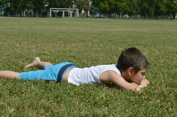 A boy in bright ,summer clothes, lying on the green grass on a clear Sunny day.