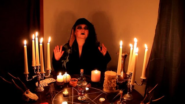 Female Fortuneteller divines in a dark room, candles are burning on a round esoteric table with a pentagram, animal skulls lie, the concept of magic, witchcraft