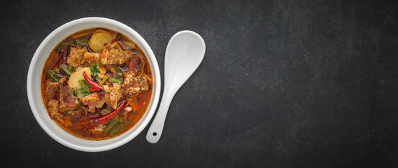 Tom Yum, Thai food, hot, spicy and sour stewed beef soup in bowl with spoon on dark gray, grey,...