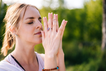 Close-up of hands of young relaxed woman with emotion of serenity and tranquility performing Namaste gesture on nature, closed eyes. Carefree yogini girl meditating on park, outside, closeup.