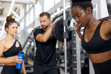 sportive people, multiethnic group perform exercises with heavy weights in gym. young diverse man and women workout, have muscular body