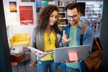 Group of happy students reading books and preparing to exam in library