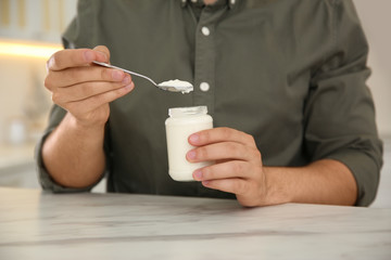 Young man with tasty yogurt at white marble table, closeup