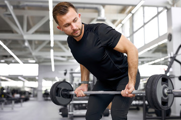 Fototapeta na wymiar caucasian athletic man pumping up muscles with barbells, strong man under physical exertion pumping up bicep muscle with heavy weight in gym