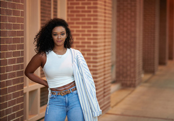 Stunning young black woman poses near brick wall wearing  blue jeans white shirt and blazer - fashion and business casual