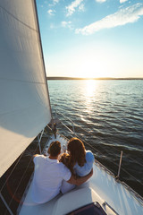 Family Of Three Sitting On Yacht Boat Deck Outdoors, Vertical