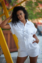 Stunning young black woman wearing white romper near a swing in a city courtyard