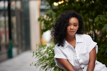 Naklejka premium Stunning young black woman poses on city sidewalk wearing white romper in summer