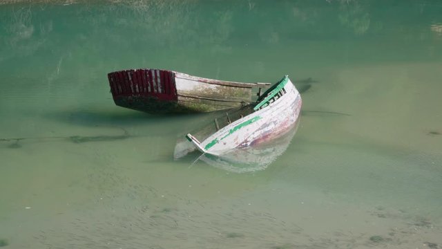 Two sunken row boats in calm teal water with fish shoal in foreground