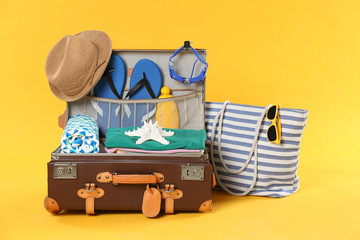 Bag and open vintage suitcase with different beach objects packed for summer vacation on orange...