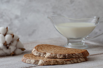 two slices of dark bread, a jug of milk, a sprig of cotton on a wooden table and a gray background...