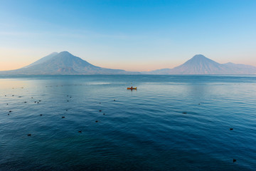 The volcanoes San Pedro, Toliman and Atitlan at sunrise by the Atitlan lake with a fisherman in a...