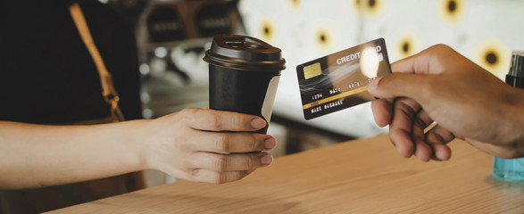 Fototapeta na wymiar Panoramic banner. customer paying with credit card for buying black coffee on counter in cafe coffee shop, cafe restaurant, digital payment, small business owner, takeaway food, food and drink concept