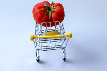 Ripe red tomato on a yellow miniature shopping cart