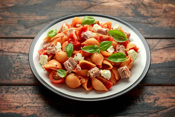 Conchiglie Tuna pasta with tomato sauce, feta cheese and basil on wooden table.
