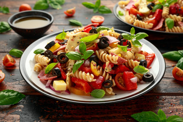 Antipasto salad with pasta, tomato, olives, red onion, bell pepper, salami, cheese, artichoke and basil.