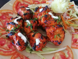 Close-up view of an Indian dish chicken Tikka tandoori, laid out on rings of tomatoes and garnished with salad