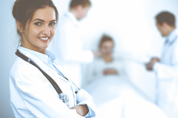 Fototapeta premium Female doctor smiling on the background with patient in the bed and two doctors