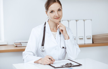 Woman-doctor sitting and working at clinic office. Portrait of female physician. Medicine concept