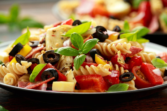 Antipasto salad with pasta, tomato, olives, red onion, bell pepper, salami, cheese, artichoke and basil.