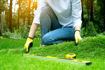 A landscape designer spreads a roll of artificial grass in a beautiful green garden