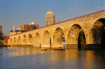 Obraz premium The Stone Arch Bridge reflected in the golden glow of sunrise on the Mississippi river at Minneapolis