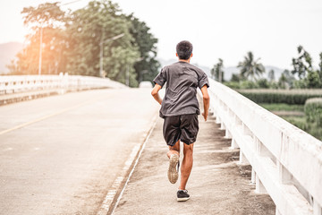 asian teenager running along the bridge in sprinting action, exercising or practicing for a...