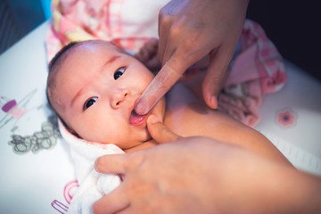 mother using finger wearing plastic baby toothbrush cleaning adorable baby tongue and mouth, parenthood motherhood raising kid child with love care kindness, keep clean hygiene looking after newborn