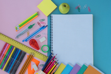 top view of school supplies and green apple  lie on blue and pink background. Copy space for text in white notebook. Back to school concept.
