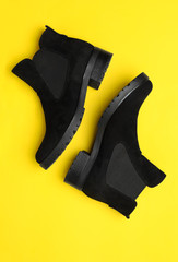 Stylish black female boots on yellow background, flat lay