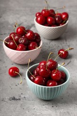 Ripe cherries in drops of water in three bowls on a gray table