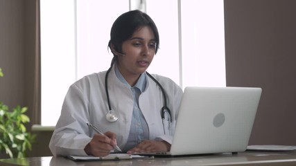 Indian telemedicine doctor wear headset consulting patient by online video call on laptop. Female gp talking with client in remote telehealth conference video chat in India. Virtual meeting visit. - Powered by Adobe